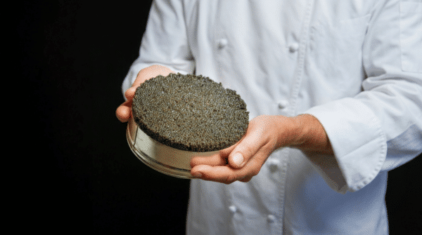 Chef en veste blanche tenant une grande boîte ouverte de caviar.