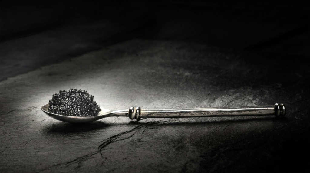 Cuillère argentée garnie de caviar Baeri noir sur une surface sombre.