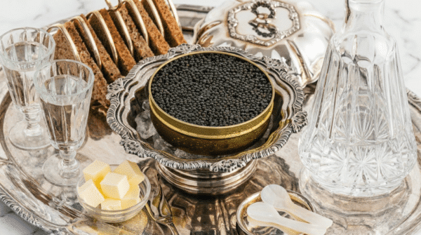 Boîte ouverte de caviar posée sur glace dans un plat en argent, accompagnée de pain, de beurre et de cuillères en nacre.